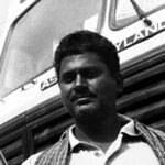 Black and white portrait of a man standing confidently in front of a truck.